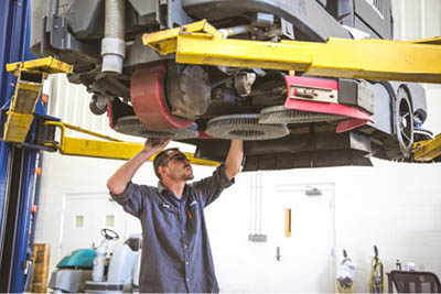 Technician repairing the scrub deck of a floor scrubber raised on a lift